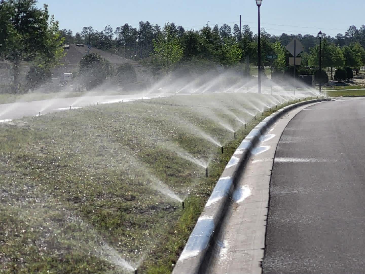 Row of sprinkler heads watering a green lawn along a curb in Spring Hill, FL